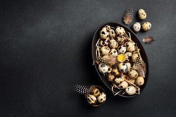 Fresh quail eggs in a black stone bowl. Quail feathers. On a black stone background. Top view.