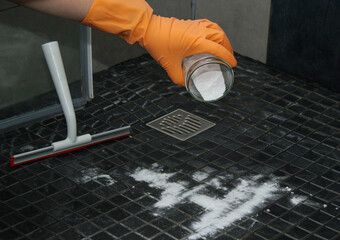 Close up of woman's hands pouring baking soda on shower floor to clean, eco friendly cleaning 