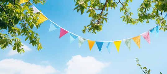 Colorful pennant string decoration in green tree foliage on blue sky, summer party background - obrazy, fototapety, plakaty