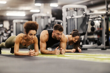 Fit sportspeople in shape are doing planks in a gym.