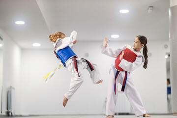 Taekwondo girl in dobok is kicking a rival and practicing combat in martial art school.