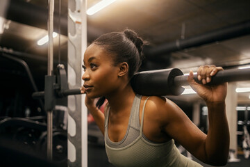 A young black sportswoman doing workouts on smith machine at gym.