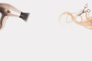 Cut wavy blonde hair, a hair dryer and scissors with copy space on the white background.