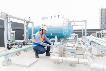 Asian male engineer working using laptop computer checks hot water pipes system or hot water boiler...