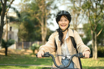 Naklejka premium Cheerful young female student in safety helmet riding a bicycle through the city park