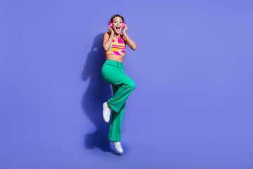 Full body length photo of youngster touching pink wireless headphones soundtrack youtube music jumping isolated on purple color background