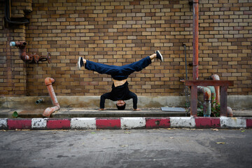 Generation Z male hip hop dancer doing cartwheel against brick wall in the city