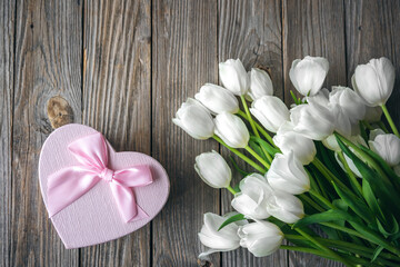 Gift box in the shape of a heart and a bouquet of tulips on a wooden background.