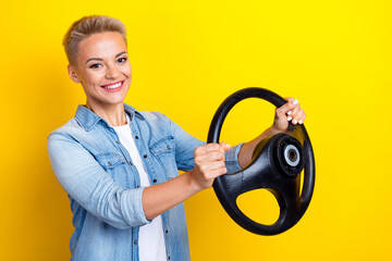 Photo portrait of pretty young girl hold steering wheel driving lesson wear trendy jeans outfit isolated on yellow color background