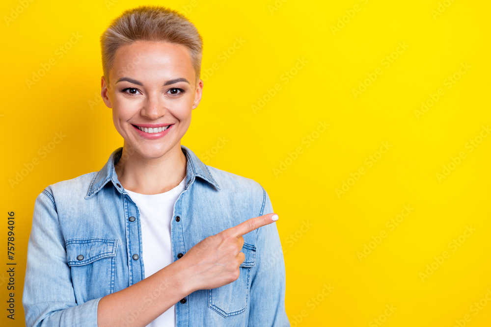 Wall mural Photo portrait of attractive young woman point empty space promo dressed stylish denim clothes isolated on yellow color background