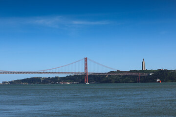 25 April Bridge and the statue of Jesus over Tagus River. Landmarks from Lisbon, Portugal, during a sunny day with blue sky.