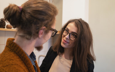 Smiling woman with glasses warmly looking at her partner, creating heartfelt and comfortable indoor atmosphere.