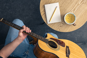A man with an acoustic guitar and a notepad with a cup on the table, top view.