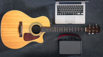 Guitar, laptop and speaker on a black background, top view.