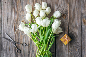 Top view, bouquet of white tulips, scissors and gift box on wooden background.