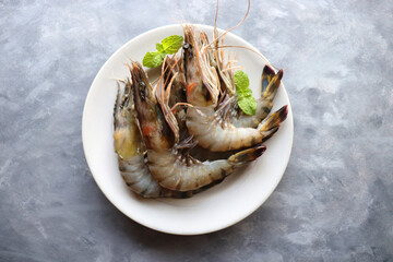 Fresh shrimp or black tiger prawns. Uncooked on a white ceramic plate with coriander and mint leaves. on a moody background with copy space. Kolambi in Marathi.