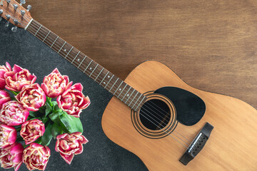 Bouquet of pink tulips and acoustic guitar on a wooden background, top view.
