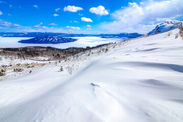 Fototapeta na wymiar 爽快な青空と雪に覆われた斜面と眼下の氷に覆われた湖。爽やかな印象の冬景色。北海道の美幌峠から見下ろす屈斜路湖。