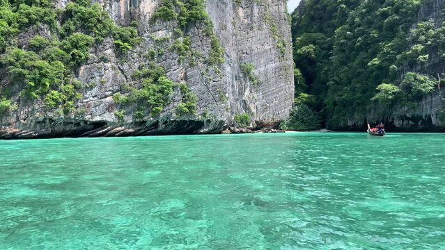 A boat peacefully glides on the tranquil waters of a lake encircled by towering mountains and lush green trees.