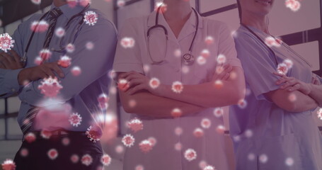 Image of macro Covid-19 cells floating on a view of a medical staff standing in the background