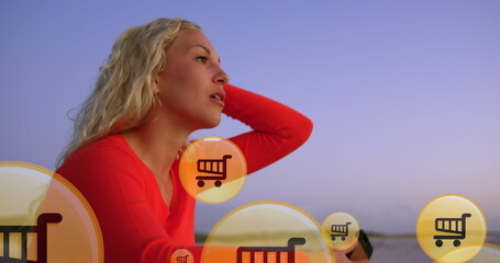 Image of shopping icons over midsection of caucasian woman using smartphone at beach