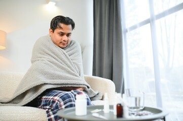 Sick Indian man in plaid sit alone shivering from cold. Unhealthy Arabian guy sit on chair feeling discomfort try to warming up