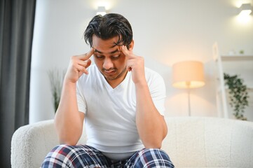 Portrait of young indian guy suffering from migraine at home, eastern man feeling unwell, touching...
