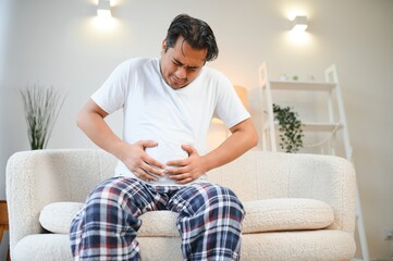 Sad exhausted guy of indian and arabian ethnicity, holds his hands on his stomach, grimaces from...