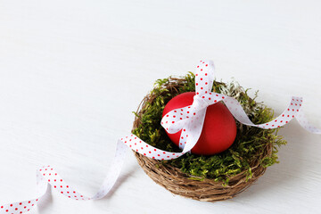 Easter card. Nest with a painted red egg with a ribbon in the nest on a white wooden background, copy space. - 757926435