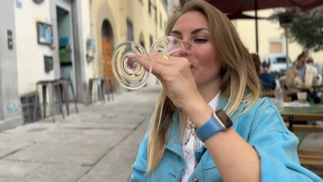 A happy woman drinks white wine or Prosecco on a terrace at a street bar in Italy 