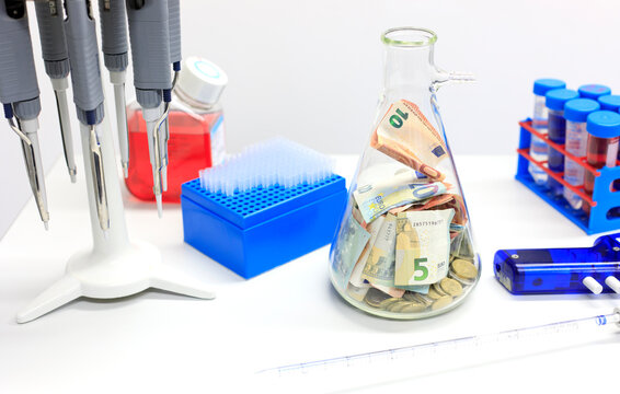 Sparschwein: Geld sparen in Wissenschaft und Forschung, Euro-Geldscheine und M&uuml;nzen in einer Laborgef&auml;&szlig;. Laborutensilien und Saugflasche Duran in Erlenmeyerform im Labor..