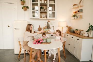 Happy mother with her daughter and son drinking tea or cocoa in the kitchen and having fun. Family communication of mom and children. Children congratulated their mother with flowers on Mother's Day.