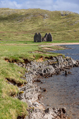 Calda House's ruins against the verdant Scottish Highlands. A rugged shoreline foregrounds the scene, leading the eye towards the historic structure, embraced by beauty of Scotland's landscapes