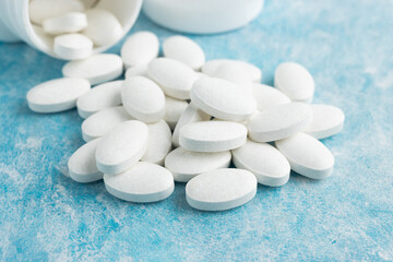 White medical pills, drugs or tablets for treatment on blue background, vitamins and minerals,...