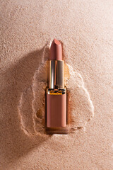 Nude matte lipstick on a sand background. Female accessory for lip makeup. Professional cosmetic product for makeup artists in the composition. Backdrop.