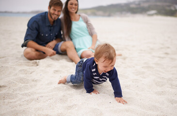 Happy, baby and parents on beach in sand, summer and family fun with child crawling. Laughing,...
