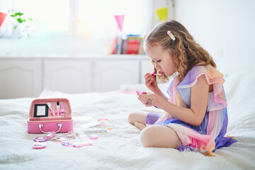 Cute preschooler girl with unicorn hair decoration playing with children cosmetic and applying makeup.