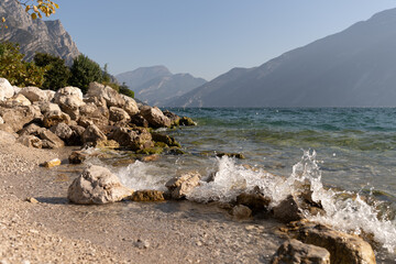 stones on the shore of a lake on a sunny day with mountains in the background