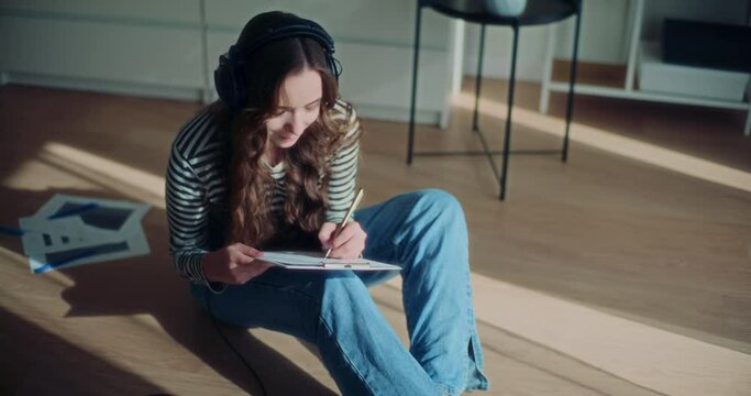 Female brunette enjoying music while drawing on clipboard