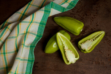 Two whole and halves of green bell pepper with green kitchen towel on wooden background. .