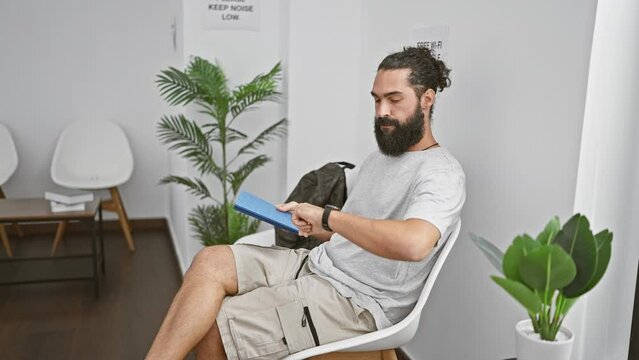 Hispanic man reading book in modern waiting room with plant decor