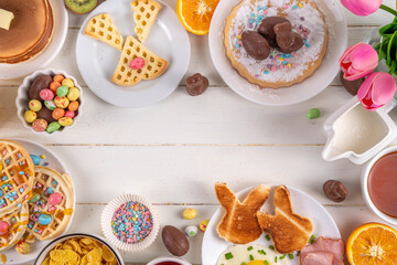 Easter holiday sweet breakfast, brunch. Easter decorated belgian waffles, pancakes, breakfast cereals and milk, fried eggs with toasts and bacon, Easter chocolate eggs and bunny, with spring flowers