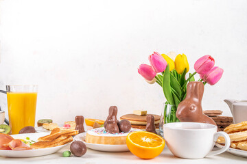 Easter holiday sweet breakfast, brunch. Easter decorated belgian waffles, pancakes, breakfast cereals and milk, fried eggs with toasts and bacon, Easter chocolate eggs and bunny, with spring flowers