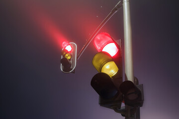 Traffic lights with red light during a foggy night.