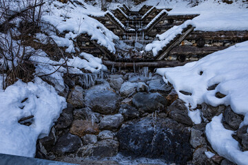 visuale di un torrente di montagna in primo piano, coperto di neve e ghiaccio, all'ombra