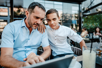 Handsome and happy father and his teenager son sitting in a restaurant and talking.