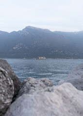 stones on the shore of a lake on a sunny day with mountains in the background and boat in the middle 