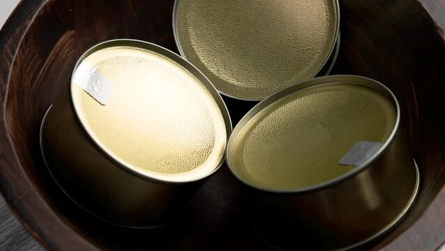 Wooden rustic bowl with new closed metallic cans of canned tuna fillet meat close up. Rotation