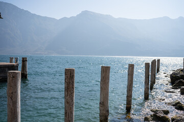 mooring posts on the embankment of a clear lake on a sunny day and mountains in the background