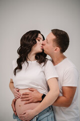 Couple waiting for baby. Family isolated on a white background. Pregnant woman and handsome man hugging tummy at home. Husband embraces belly wife. Nine months. Loving couple kissing embrace together.